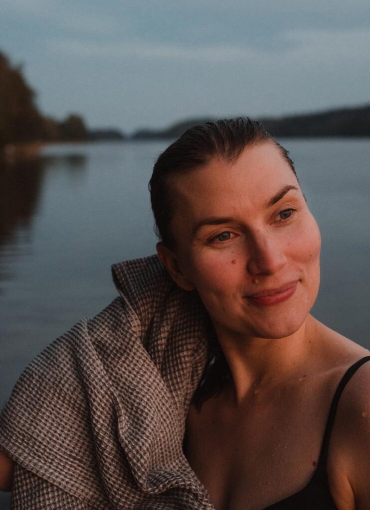 A woman enjoying a refreshing swim beside the UNA Design Sauna by Desavu at a waterfront resort in Finland